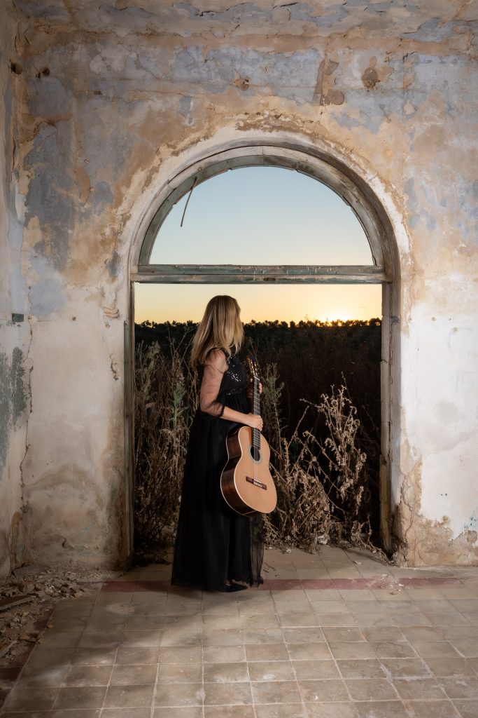 Laura Verdugo del Rey con guitarra clásica mirando el horizonte en espacio arquitectónico con arco