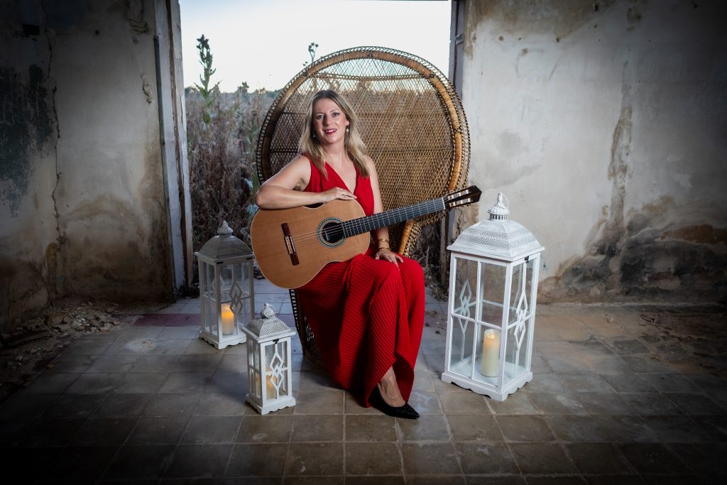 Laura Verdugo del Rey con guitarra clásica sentada con vestido rojo en entorno arquitectónico histórico