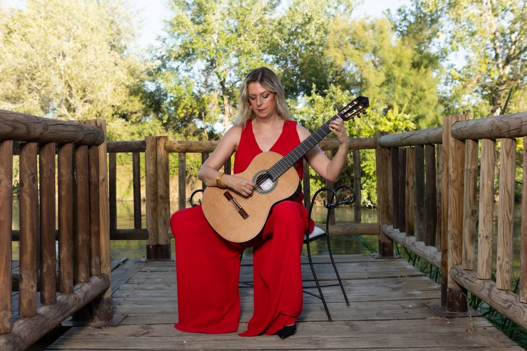 Laura Verdugo del Rey interpretando guitarra clásica en pasarela de madera en entorno natural